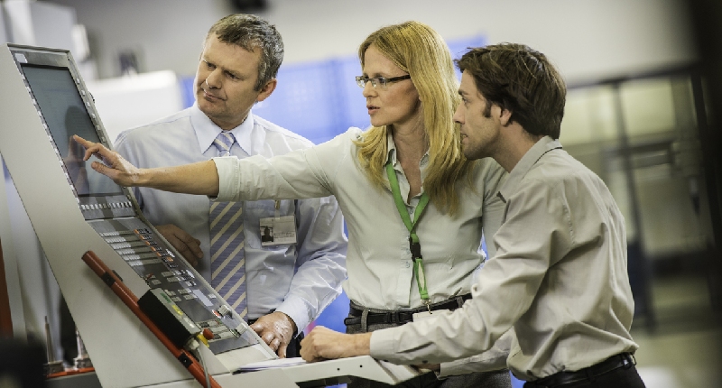 a group of engineers standing around a CNC machine